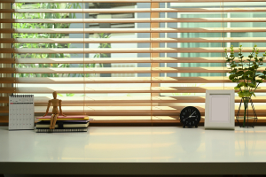 Home office desk with calendar, books, alarm clock, potted plant and picture frame with timber venetian blinds on the window